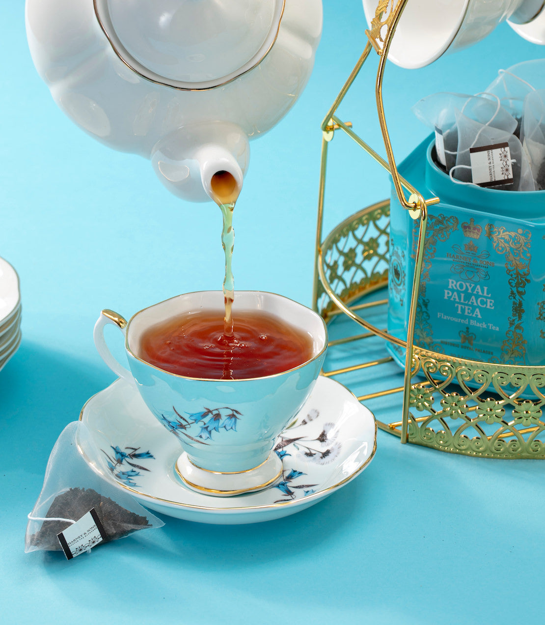 Tea being poured from a teapot into a decorative teacup on a blue background with Royal Palace Tea tea tin.