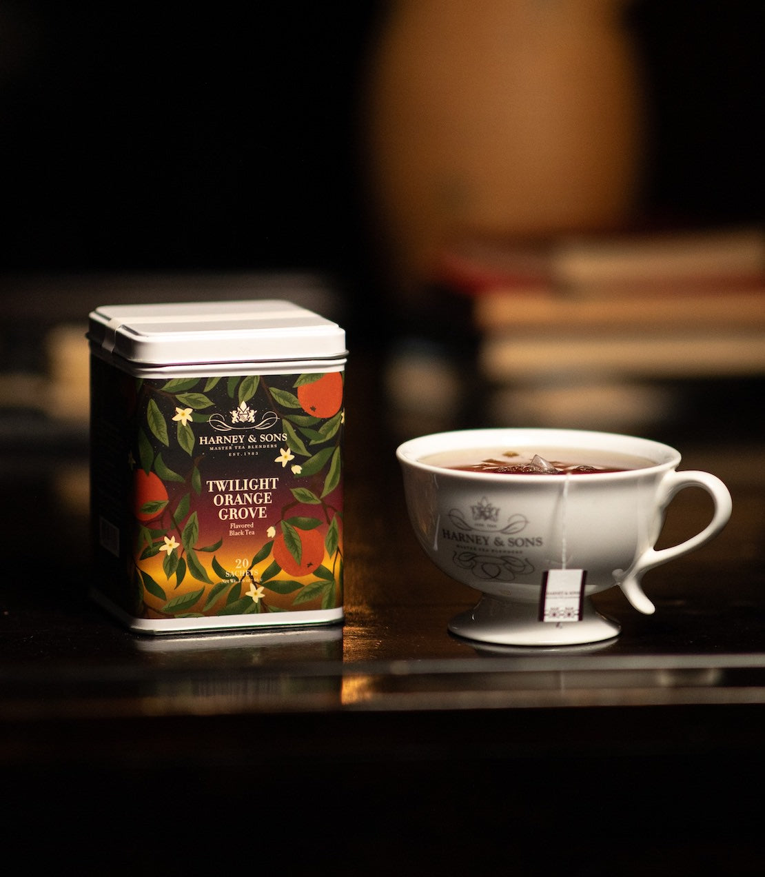 Harney & Sons Fine Tea Twilight Orange Grove Flavored Black Tea tin of 20 sachets mood shot pictured with Harney & Sons logo cup and bowl of oranges