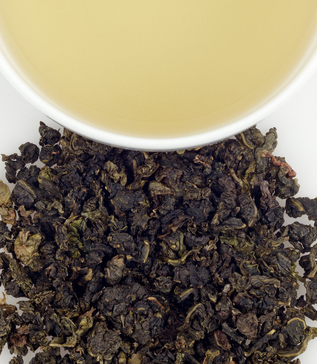Milky Oolong tea leaves beside a cup of brewed tea, showcasing its rich color and unique texture.