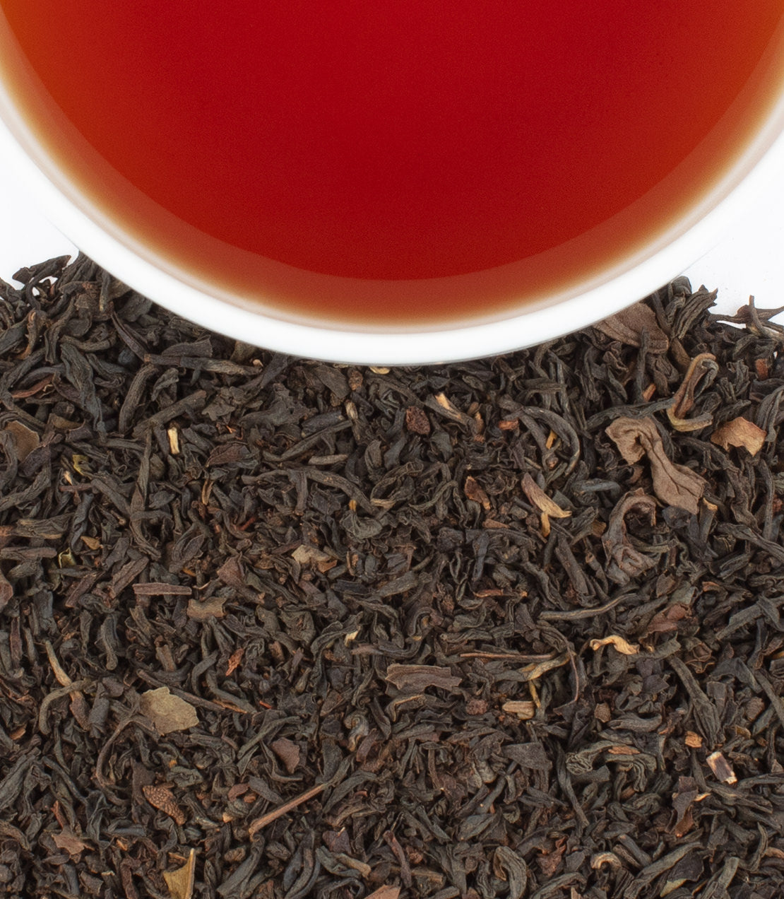 Earl Grey tea sachets in a tin, with brewed tea in a cup and loose tea leaves scattered below.