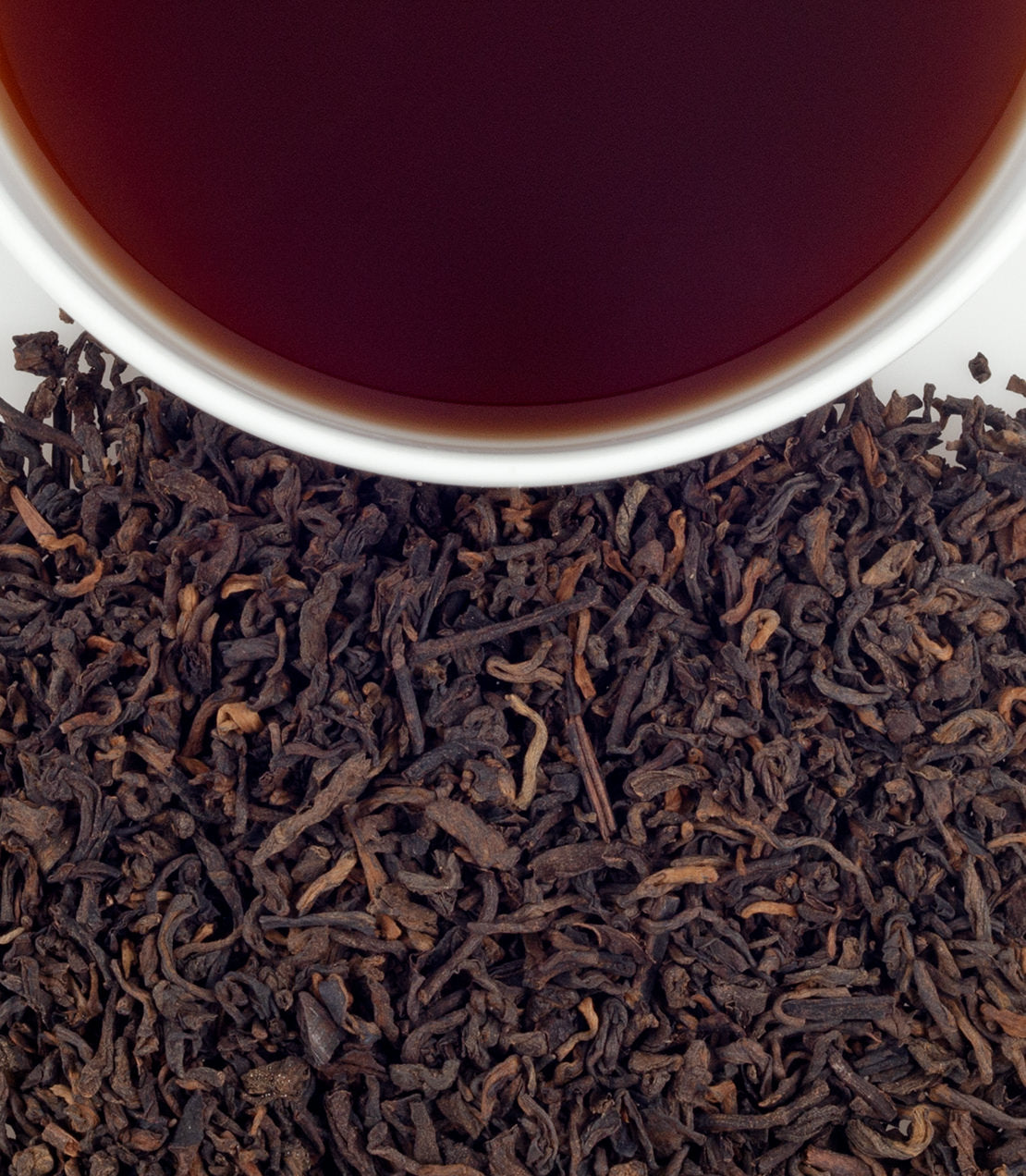 Pu-erh tea sachets in a bag, with loose tea leaves and a cup of brewed tea above. Rich, dark color.