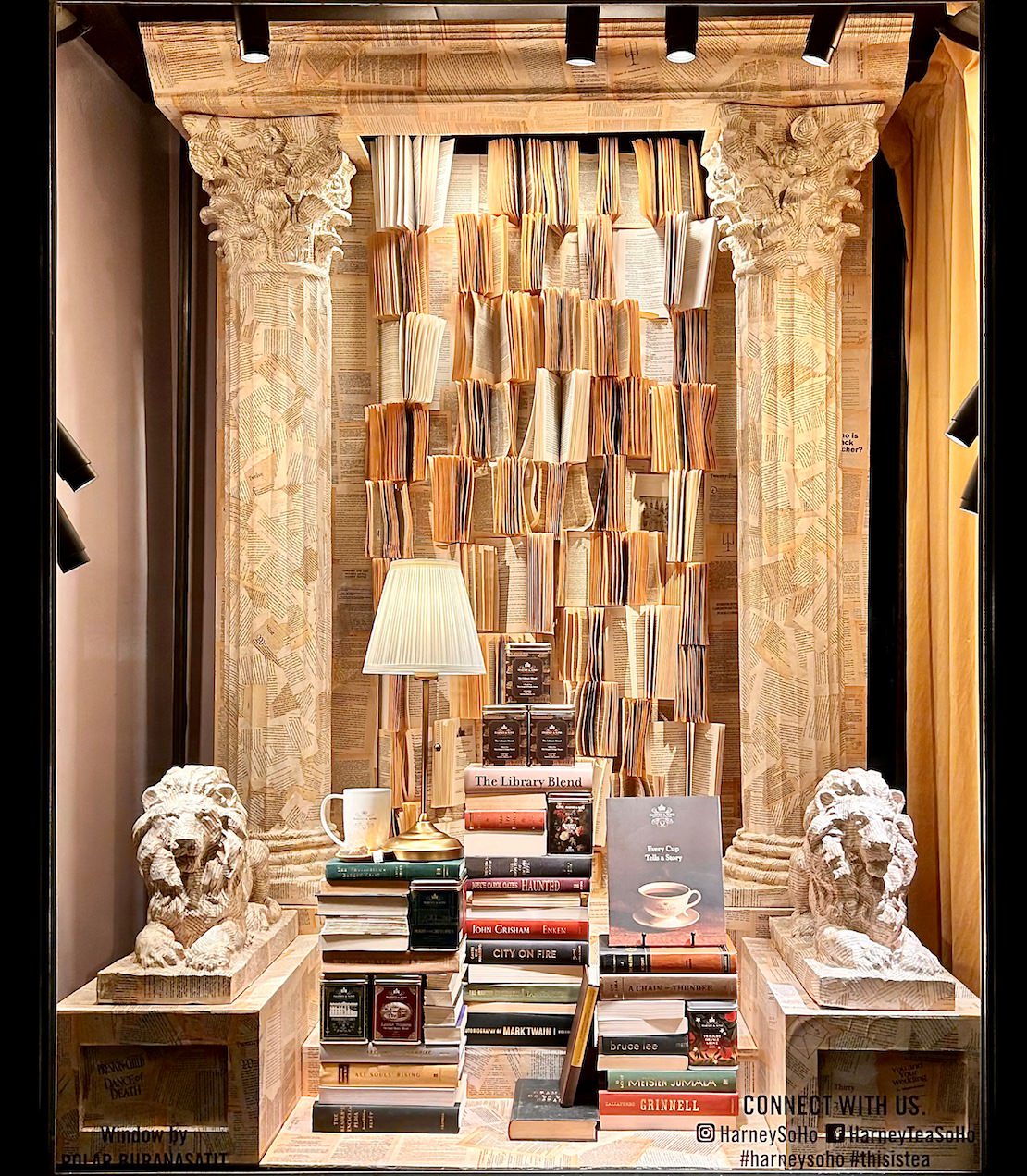 Harney & Sons SoHo store window with decorative books and a lamp, framed by classical architecture elements inspired by the facade of the New Your Public Library. 
