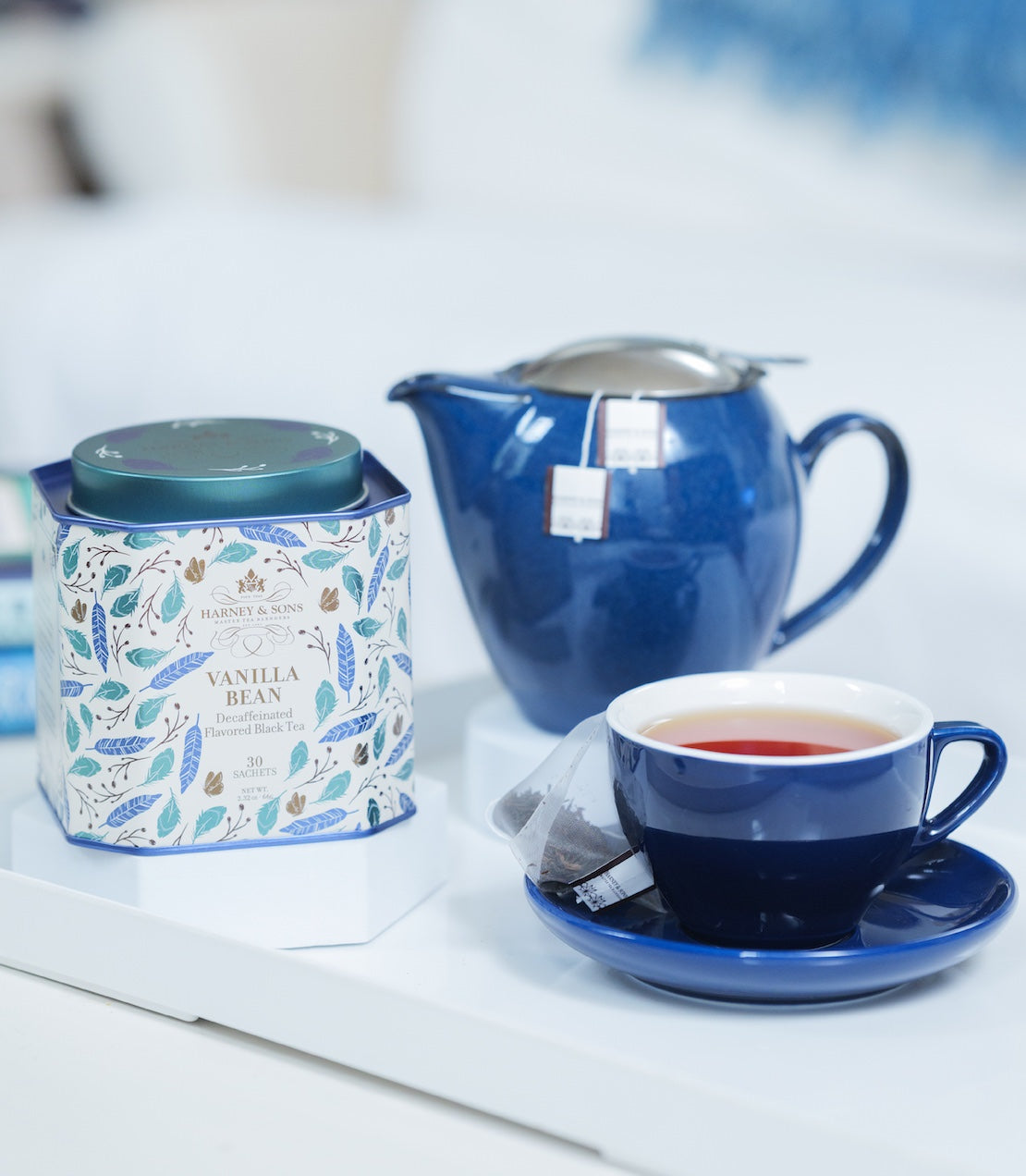 Tea set with a blue teapot, cup, and Vanilla Bean tea tin on a white surface.