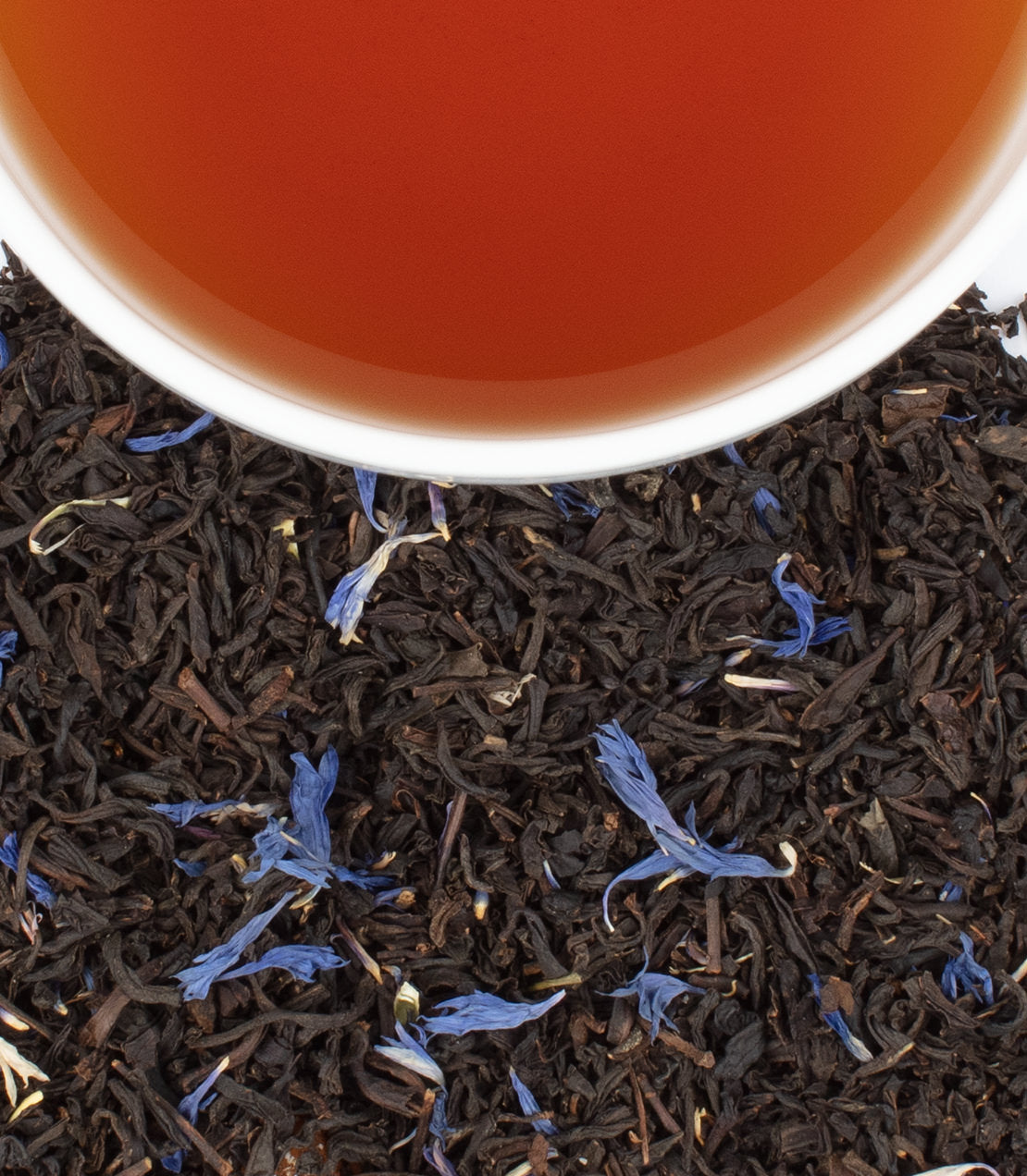 Celebration Tea sachets with brewed tea in a cup, surrounded by loose black tea and blue flower petals.